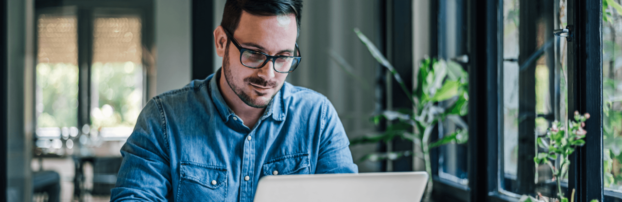 Guy sitting at desk with computer writing in notebook